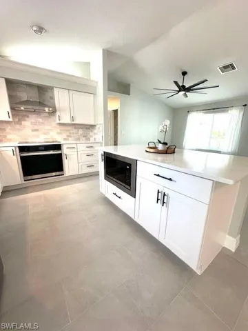 Kitchen with oven, built in microwave, ceiling fan, wall chimney range hood, and visible vents