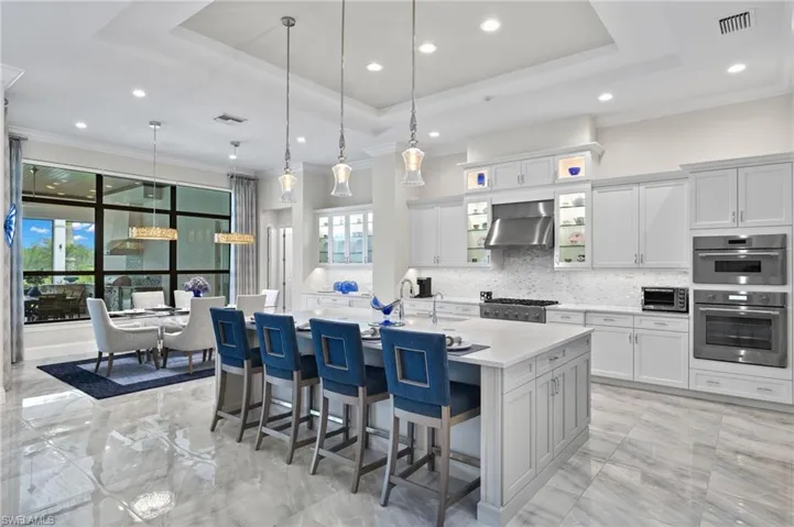 Kitchen with hanging light fixtures, backsplash, an island with sink, wall chimney exhaust hood, and stainless steel appliances
