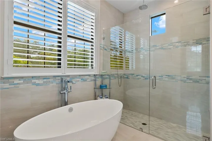 Bathroom with tile walls,  tile floors, and separate shower with frameless door and tub
