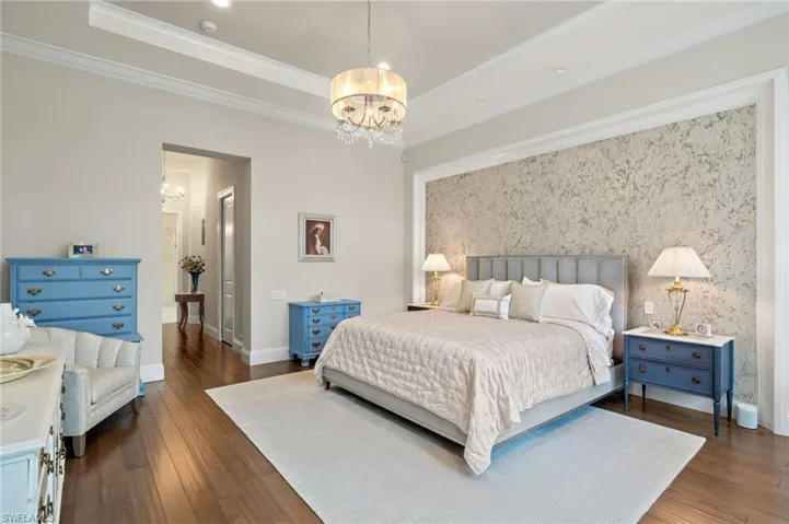 Bedroom with crown molding, a raised ceiling, a chandelier, and hardwood style floors