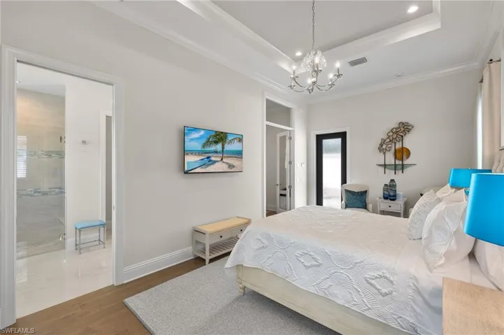 Bedroom featuring hardwood style floors, a raised ceiling, a chandelier, connected bathroom, and ornamental molding