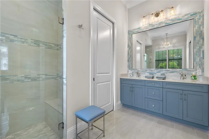 Bathroom with vanity, decorative backsplash, a chandelier, and a step down shower with frameless door
