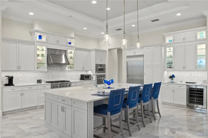 Kitchen with wall range hood, appliances with stainless steel finishes, white cabinets, wine cooler, and decorative backsplash