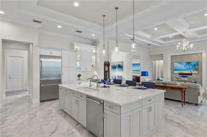 Kitchen featuring sink, coffered ceiling, stainless steel appliances, white cabinets, and a center island with sink