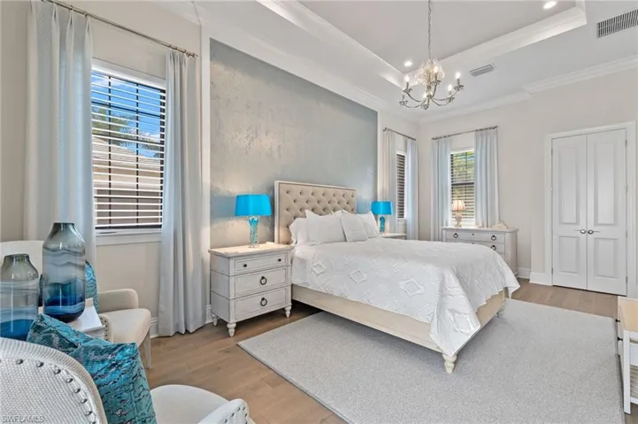 Bedroom with an inviting chandelier, light hardwood flooring, ornamental molding, and a tray ceiling