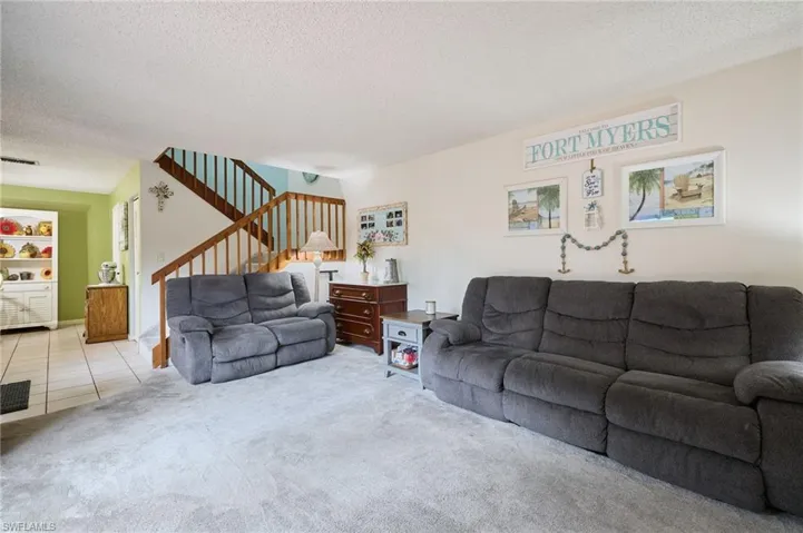 Carpeted living room featuring a textured ceiling, stairway, and tile patterned flooring