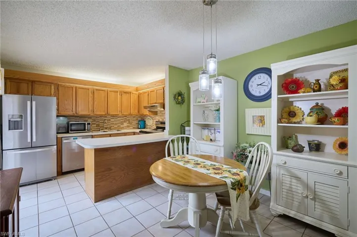 Kitchen featuring a textured ceiling, appliances with stainless steel finishes, light tile patterned floors, light countertops, and a peninsula