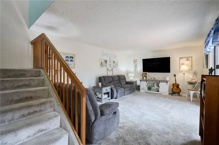 Carpeted living area with a textured ceiling and stairway