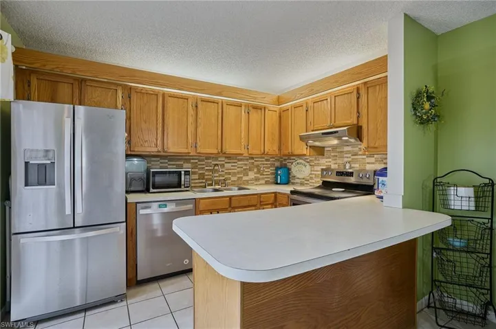 Kitchen with appliances with stainless steel finishes, a peninsula, light tile patterned flooring, backsplash, and a textured ceiling
