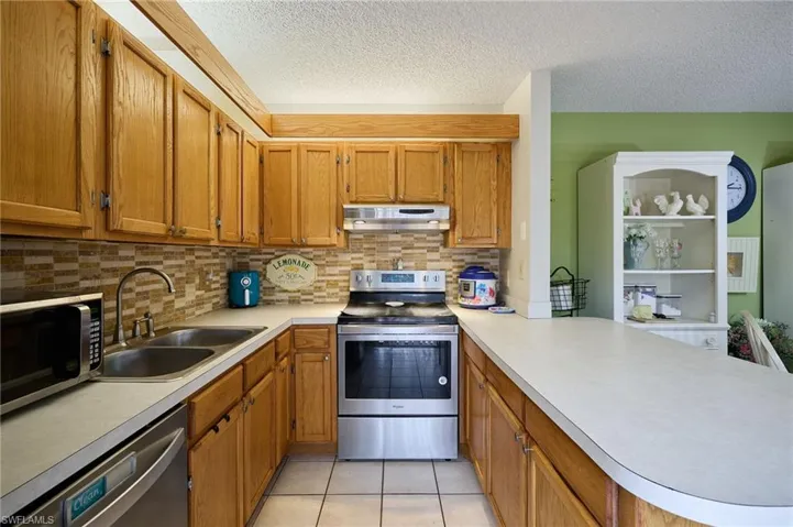 Kitchen featuring appliances with stainless steel finishes, brown cabinets, backsplash, light tile patterned flooring, and light countertops