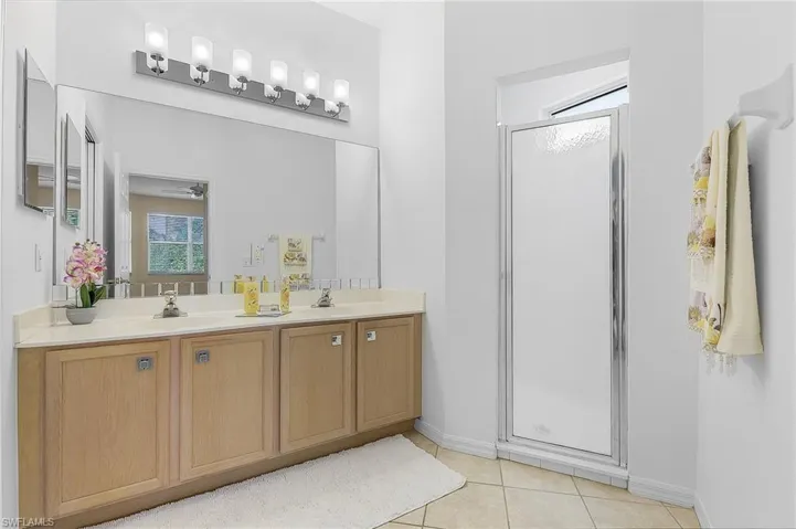 Bathroom with vanity, walk in shower, ceiling fan, and tile patterned flooring