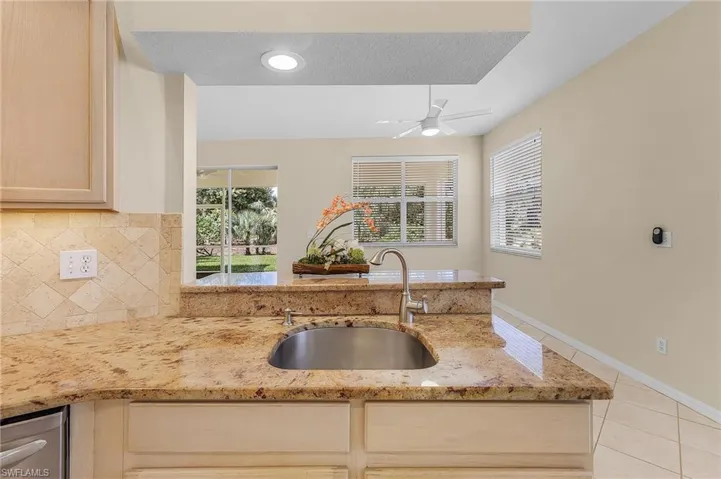 Kitchen featuring light stone counters, sink, ceiling fan, decorative backsplash, and a textured ceiling