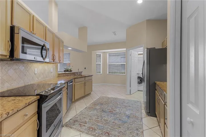 Kitchen featuring light brown cabinetry, appliances with stainless steel finishes, decorative backsplash, and light tile patterned flooring