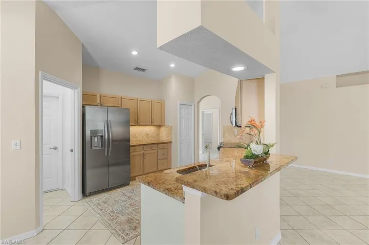 Kitchen with sink, stainless steel fridge, kitchen peninsula, light tile patterned flooring, and tasteful backsplash