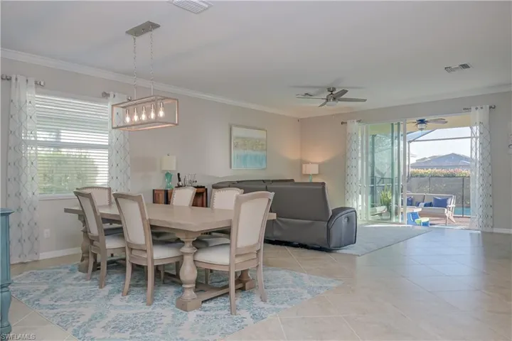Dining space with ceiling fan with notable chandelier, light tile flooring, a wealth of natural light, and ornamental molding