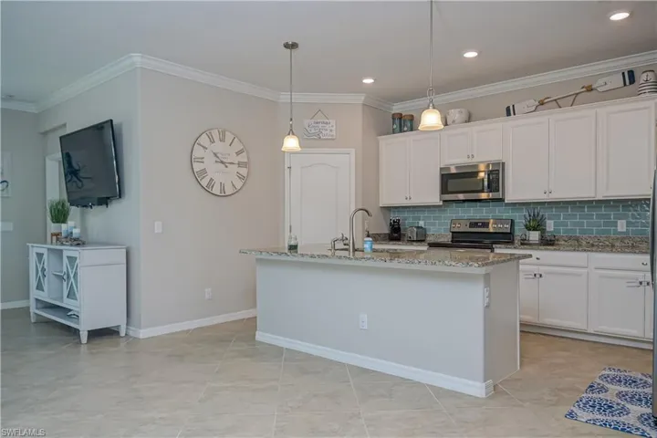 Kitchen featuring tasteful backsplash, stainless steel appliances, pendant lighting, white cabinets, and a kitchen island with sink