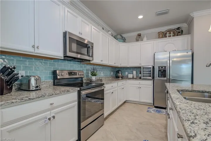Kitchen with ornamental molding, light tile flooring, backsplash, and appliances with stainless steel finishes