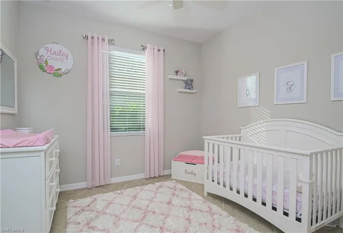 Bedroom featuring a nursery area, light tile flooring, and ceiling fan