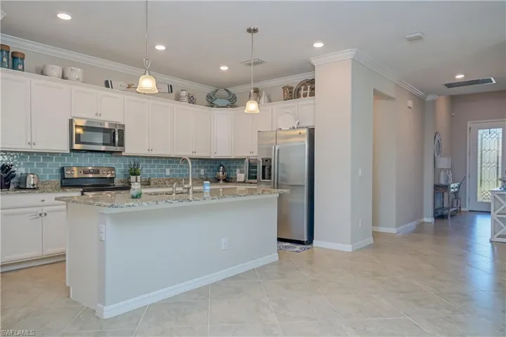 Kitchen featuring appliances with stainless steel finishes, white cabinets, tasteful backsplash, and an island with sink