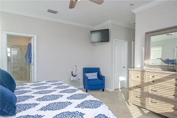 Bedroom featuring ceiling fan, ensuite bathroom, crown molding, and light tile floors