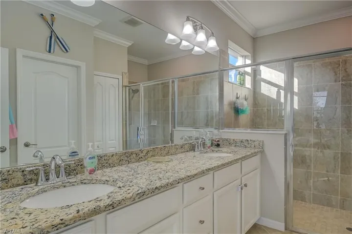 Bathroom featuring dual vanity, walk in shower, and ornamental molding
