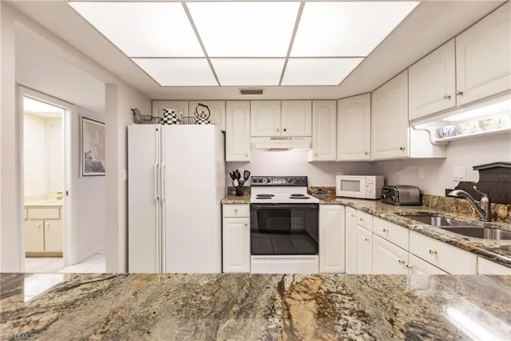 Kitchen featuring white cabinetry, sink, dark stone counters, and white appliances