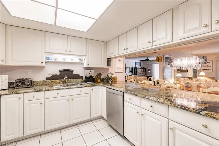 Kitchen with dishwasher, white cabinets, ceiling fan with notable chandelier, sink, and light tile patterned flooring