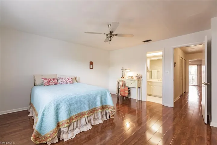 Bedroom with dark hardwood / wood-style flooring, ceiling fan, and connected bathroom