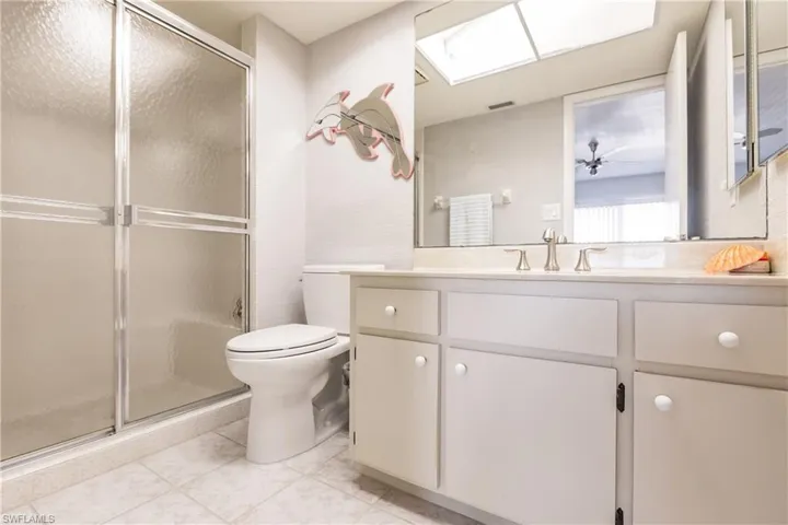 Bathroom with vanity, a shower with door, ceiling fan, tile patterned flooring, and toilet