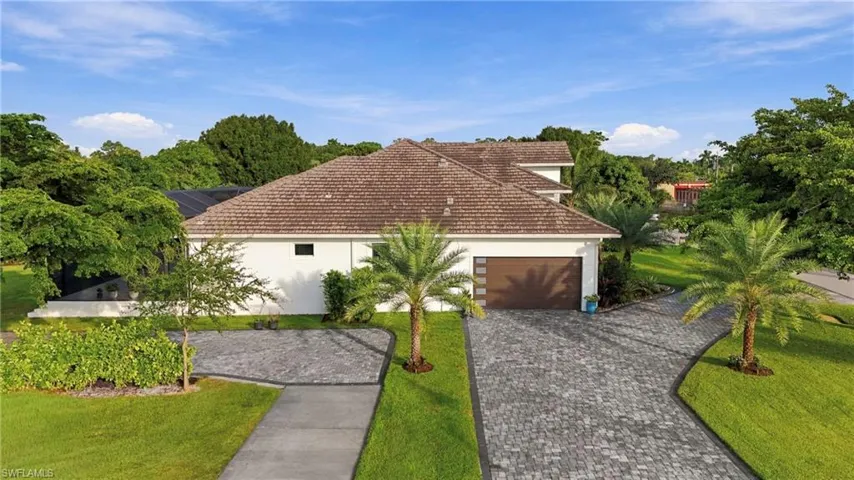 Single-story exterior featuring a hip roof, stucco facade, paver driveway, attached multi-car garage, and established landscape