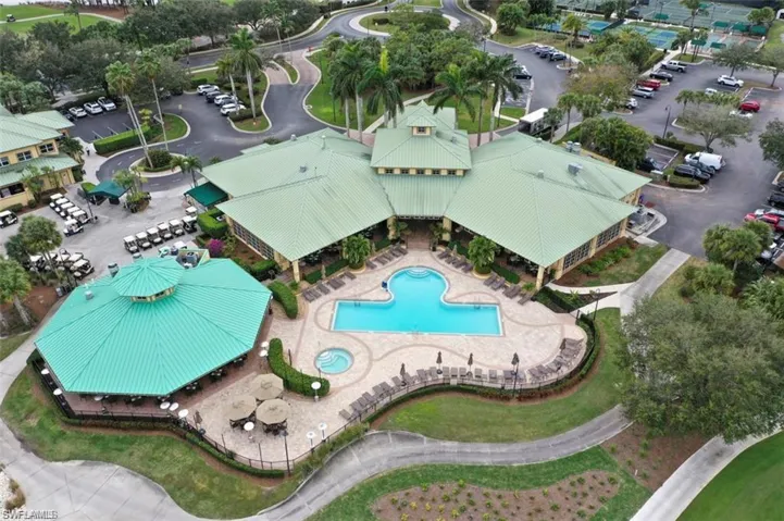 Community clubhouse featuring a metal roof, outdoor swimming pool, integrated spa, paved sun deck, and surrounding lush landscaping