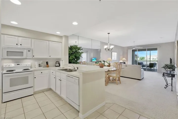 Kitchen featuring white appliances, light countertops, pendant lighting, light carpet, and white cabinets