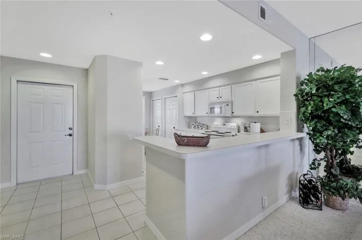 Kitchen featuring recessed lighting, light countertops, a peninsula, white cabinetry, and white appliances