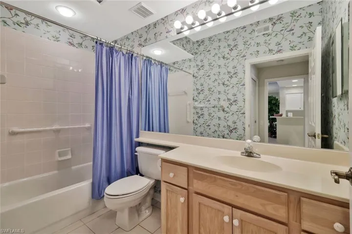 Bathroom with light tile patterned floors, shower / bathtub combination with curtain, vanity, and wallpapered walls