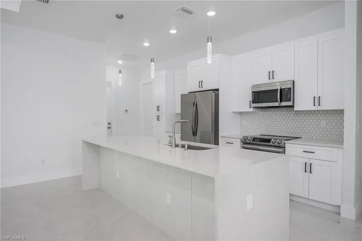 Kitchen with light stone countertops, stainless steel appliances, white cabinetry, a center island with sink, and pendant lighting