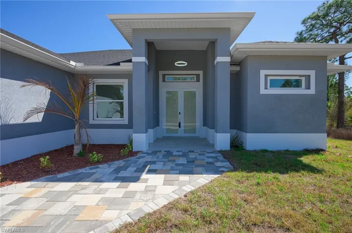 Entrance to property with french doors, stucco siding, and a lawn