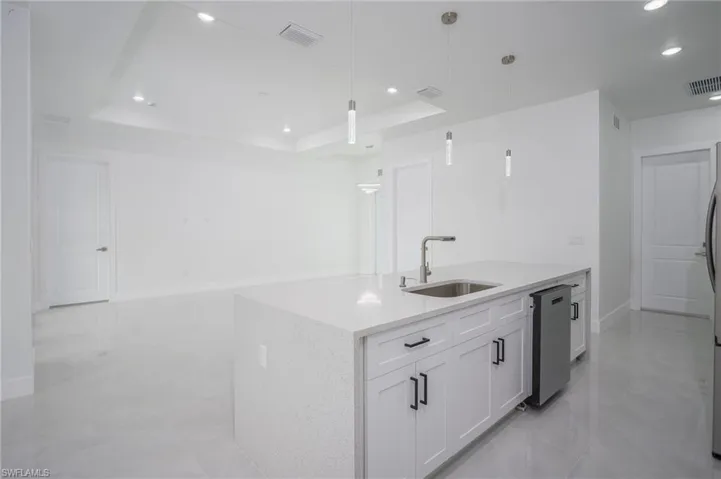 Kitchen featuring white cabinets, light stone countertops, dishwasher, hanging light fixtures, and a tray ceiling