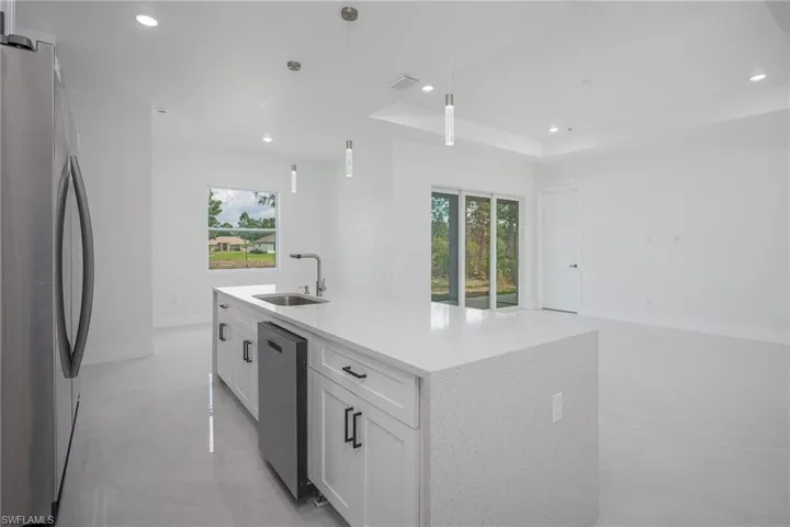 Kitchen with white cabinetry, stainless steel appliances, light stone counters, an island with sink, and plenty of natural light