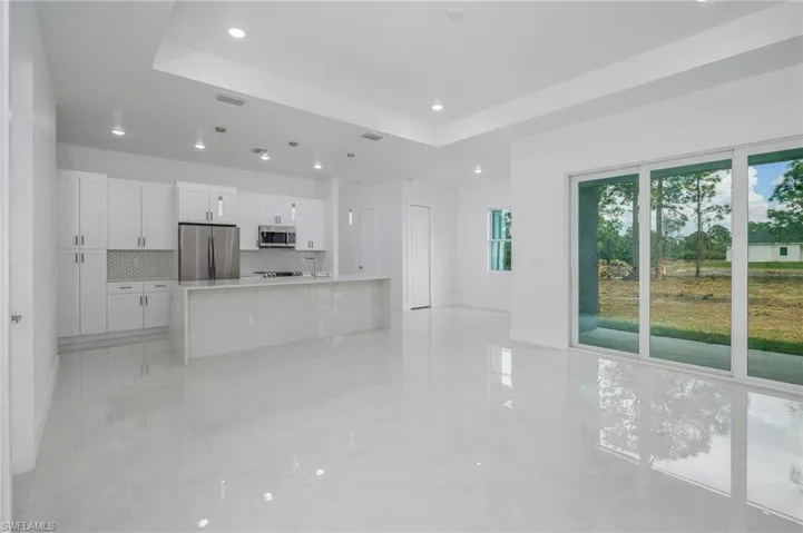 Kitchen with white cabinets, stainless steel appliances, a center island with sink, a raised ceiling, and recessed lighting