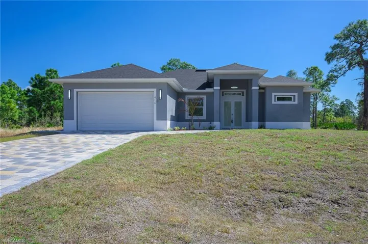 Prairie-style home with a front lawn, driveway, a garage, stucco siding, and french doors