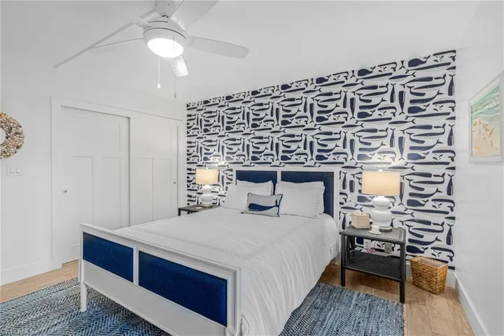 Bedroom with an accent wall, light wood-type flooring, a ceiling fan, a closet, and wallpapered walls
