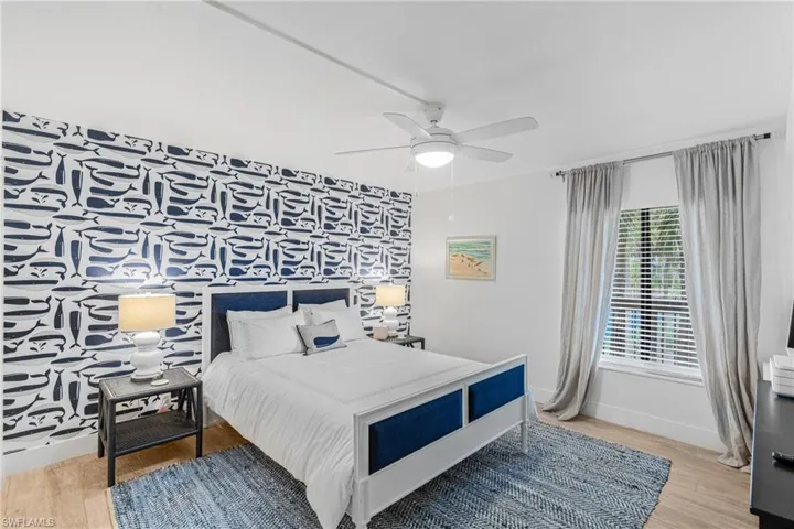 Bedroom with an accent wall, light wood finished floors, a ceiling fan, and wallpapered walls
