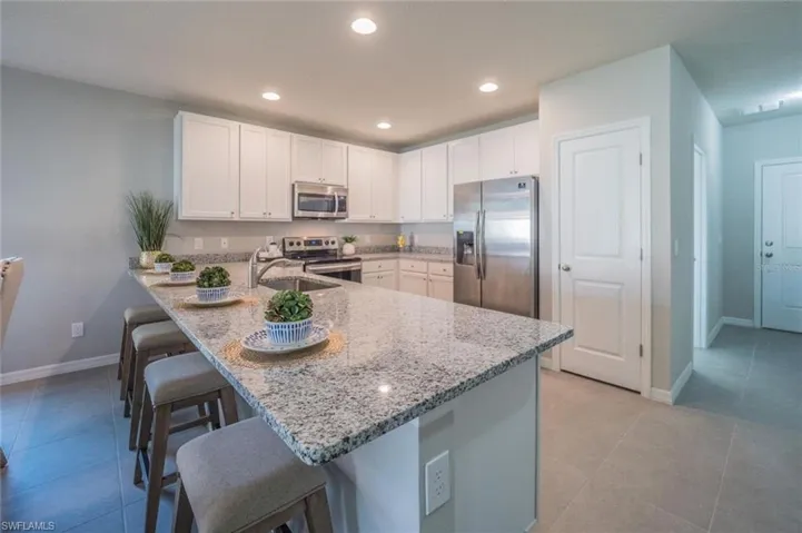 Kitchen with a peninsula, stainless steel appliances, a kitchen breakfast bar, white cabinets, and light stone counters