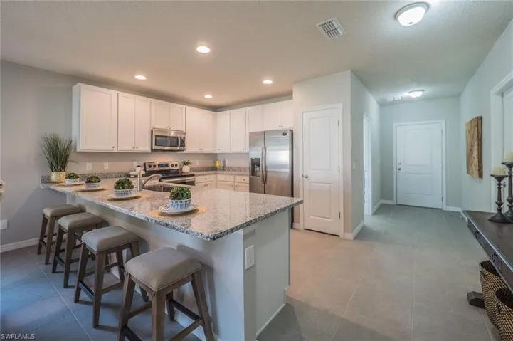 Kitchen featuring white cabinetry, a peninsula, a kitchen bar, light stone counters, and stainless steel appliances