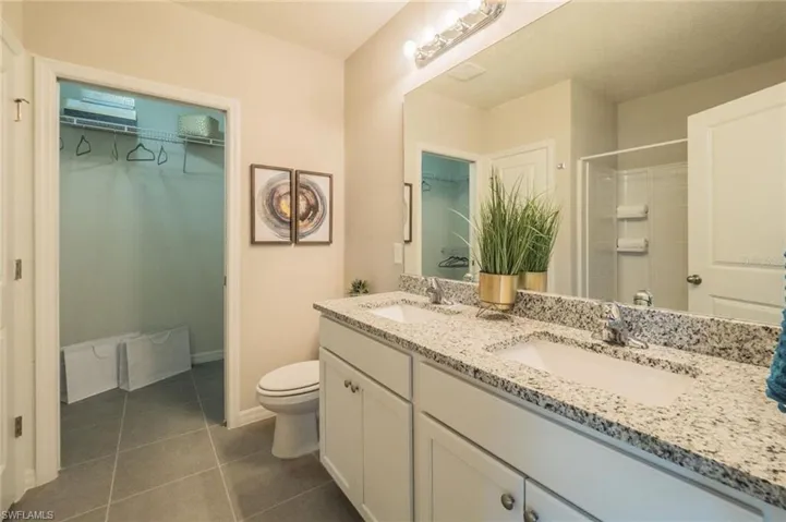 Bathroom with double vanity, a spacious closet, dark tile patterned flooring, and a shower