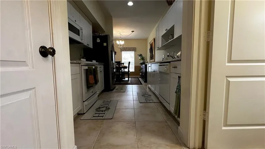 Kitchen with white cabinetry, a chandelier, hanging light fixtures, white appliances, and light tile patterned floors