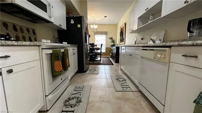 Kitchen featuring white cabinetry, stone counters, white appliances, an inviting chandelier, and light tile patterned floors