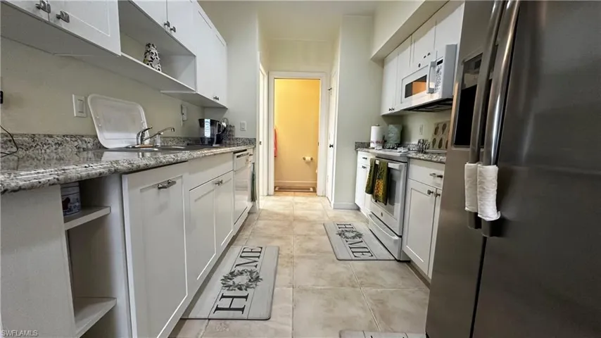 Kitchen with white cabinets, white appliances, sink, light tile patterned floors, and light stone countertops