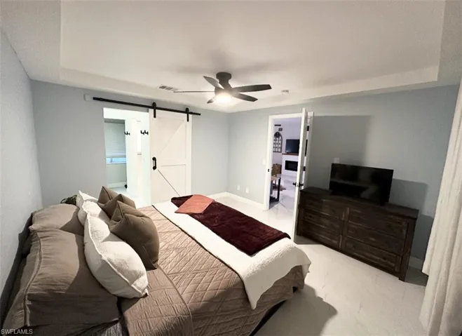 Bedroom featuring a walk in closet, a tray ceiling, a barn door, ensuite bathroom, and ceiling fan
