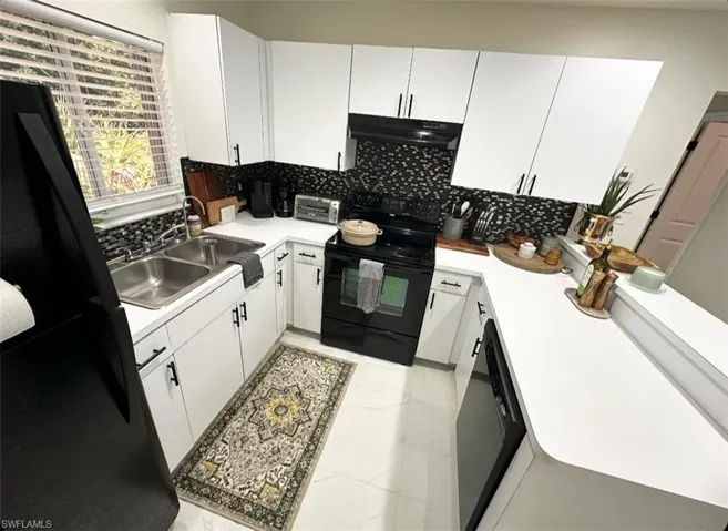 Kitchen featuring black appliances, backsplash, light tile floors, sink, and white cabinets